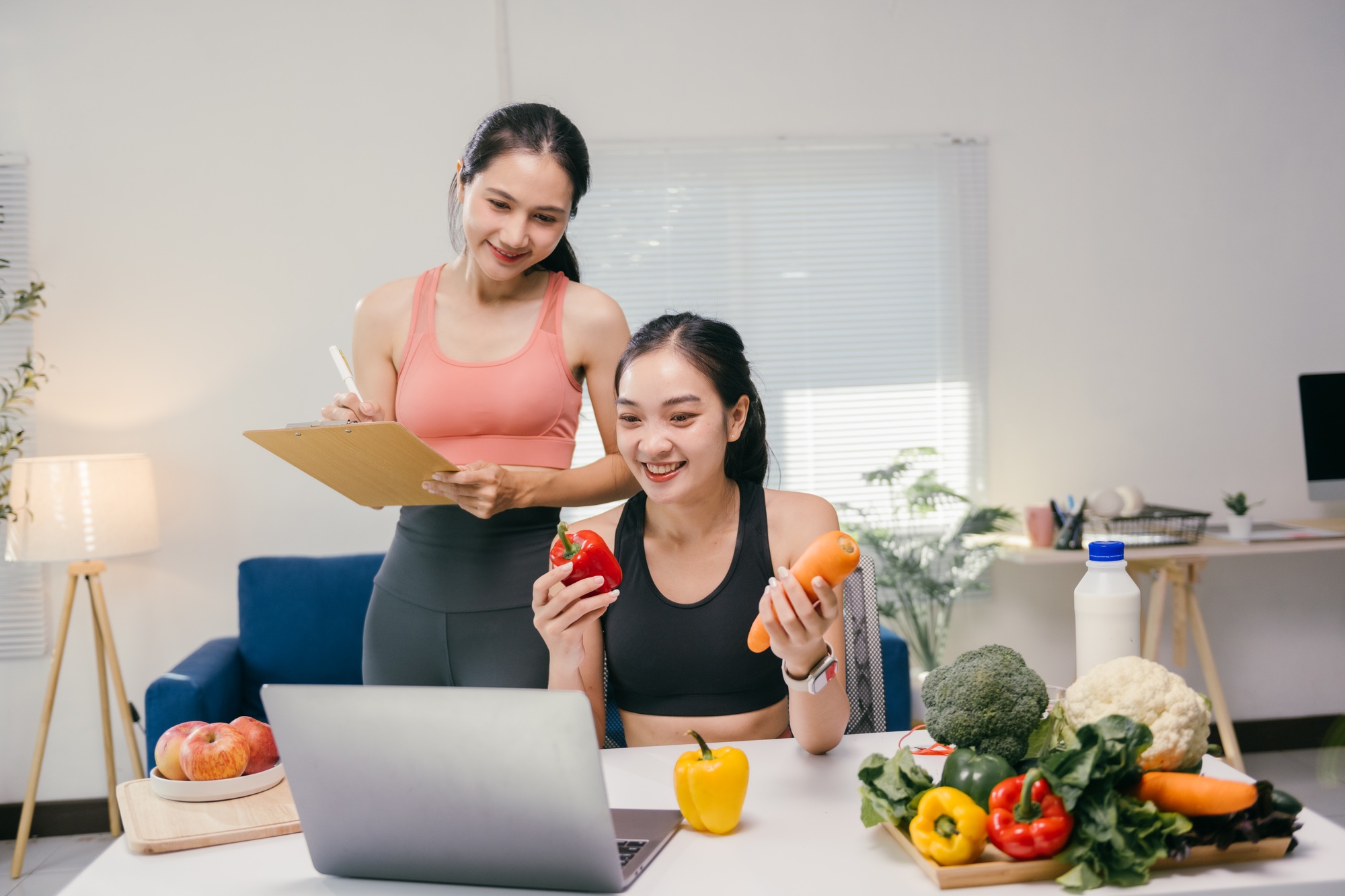 Nutritionist writing on clipboard while coaching a woman online about healthy eating, with various v